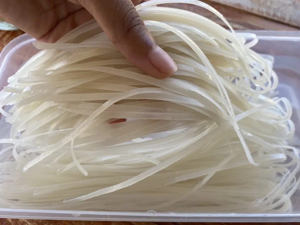 Holding dried rice noodles that are soaked in water with 1 hand.