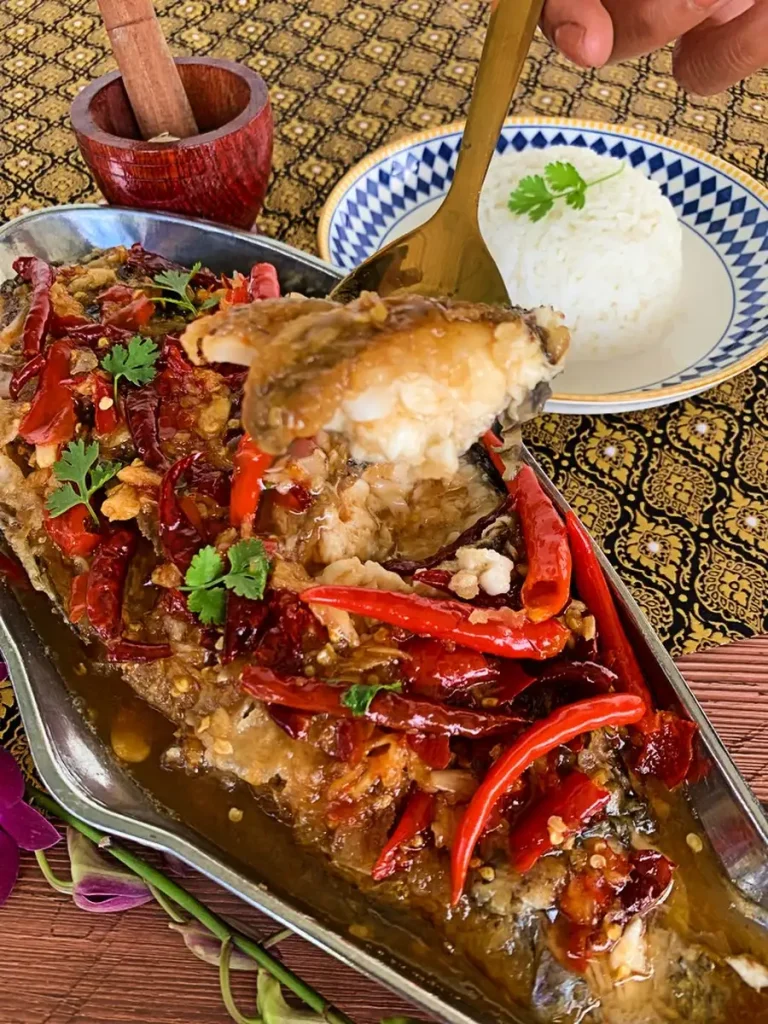 Thai crispy fish with tamarind sauce drenched in a sweet and spicy sauce, garnished with red chilies and cilantro, served with jasmine rice.