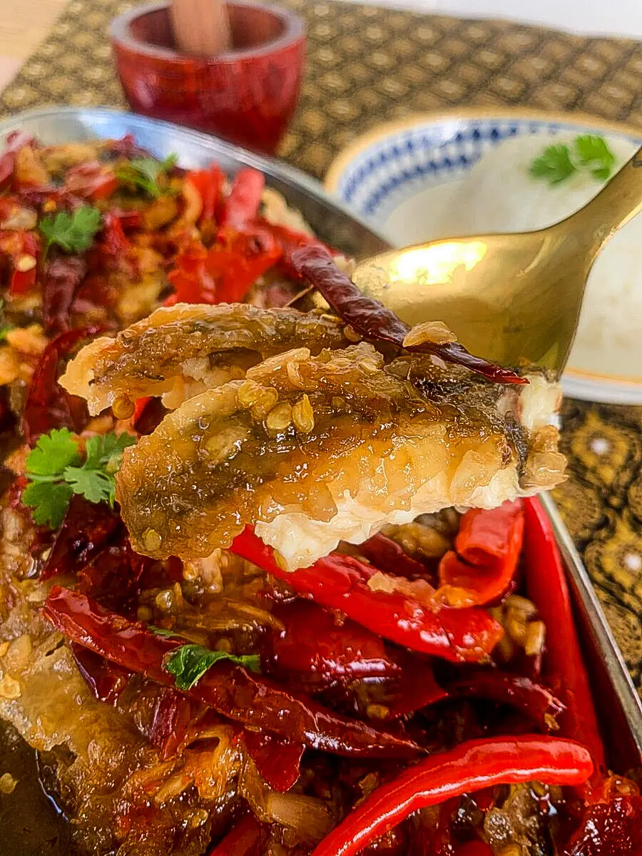 Thai fried fish topped with sticky tamarind sauce, garlic, and dried red chilies, served with steamed rice in the background.