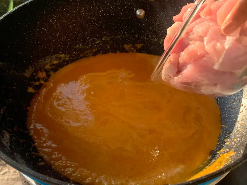 Wok with coconut curry sauce and glass bowl with sliced pork.