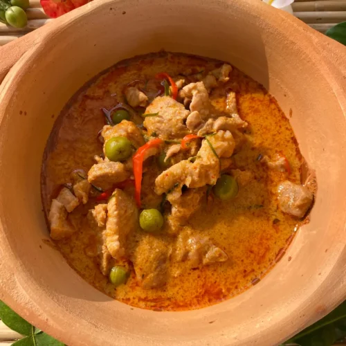 Authentic panang curry in a clay soup dish with pork, red chilies, and snow peas.