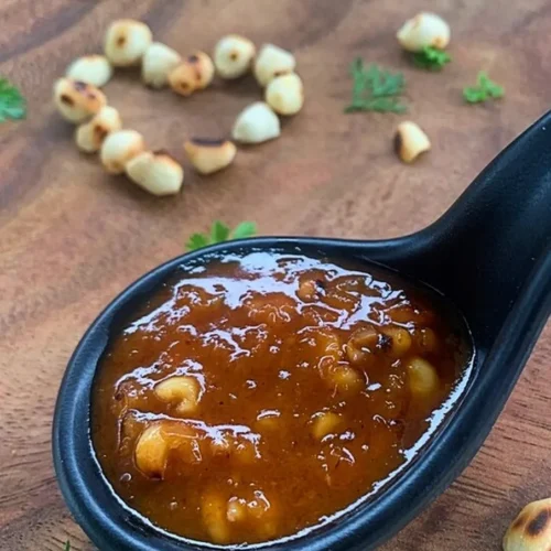 Authentic Thai peanut sauce with coconut milk in a black spoon on a wooden background, garnished with roasted peanuts and fresh cilantro.