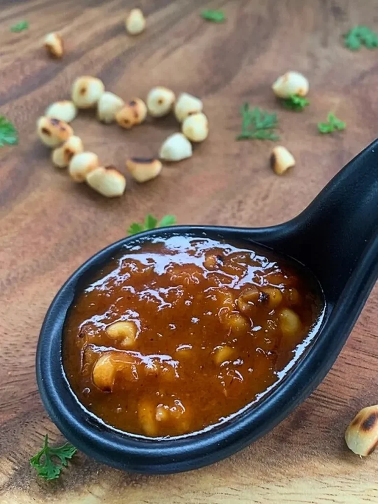 Authentic Thai peanut sauce with coconut milk in a black spoon on a wooden background, garnished with roasted peanuts and fresh cilantro.