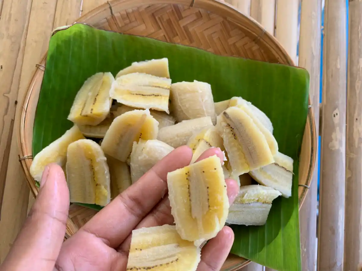 Hand holding sliced bananas over a bamboo dish with more banana slices.