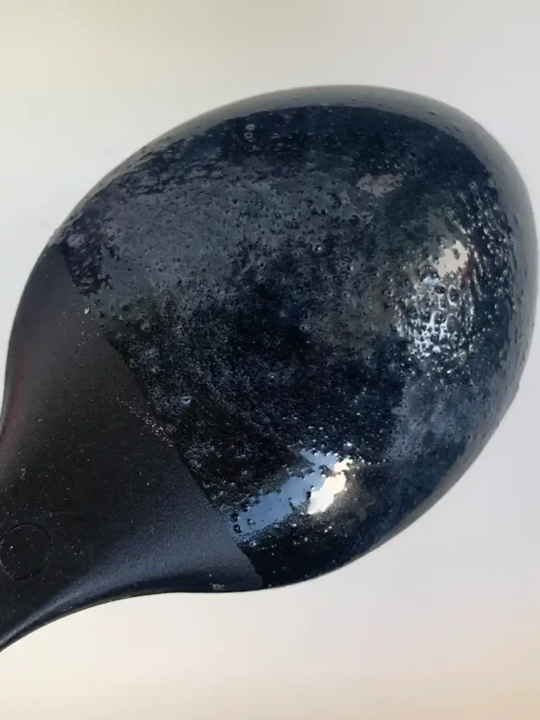 Backside of a large black plastic spoon with traces of agar-agar powder.