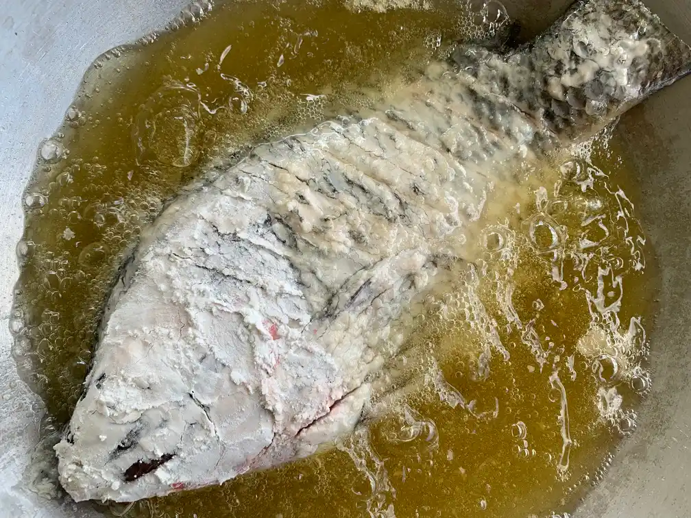 Close-up of a whole fish being deep-fried in a wok pan.