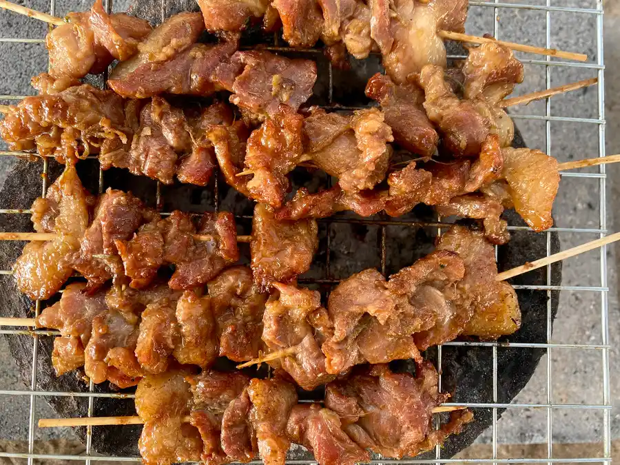 Several moo ping (Thai grilled pork skewers) on a grill over charcoal.