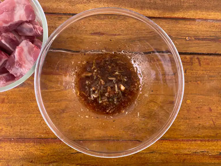 Glass bowl on wooden table with marinade mixture ready for meat.