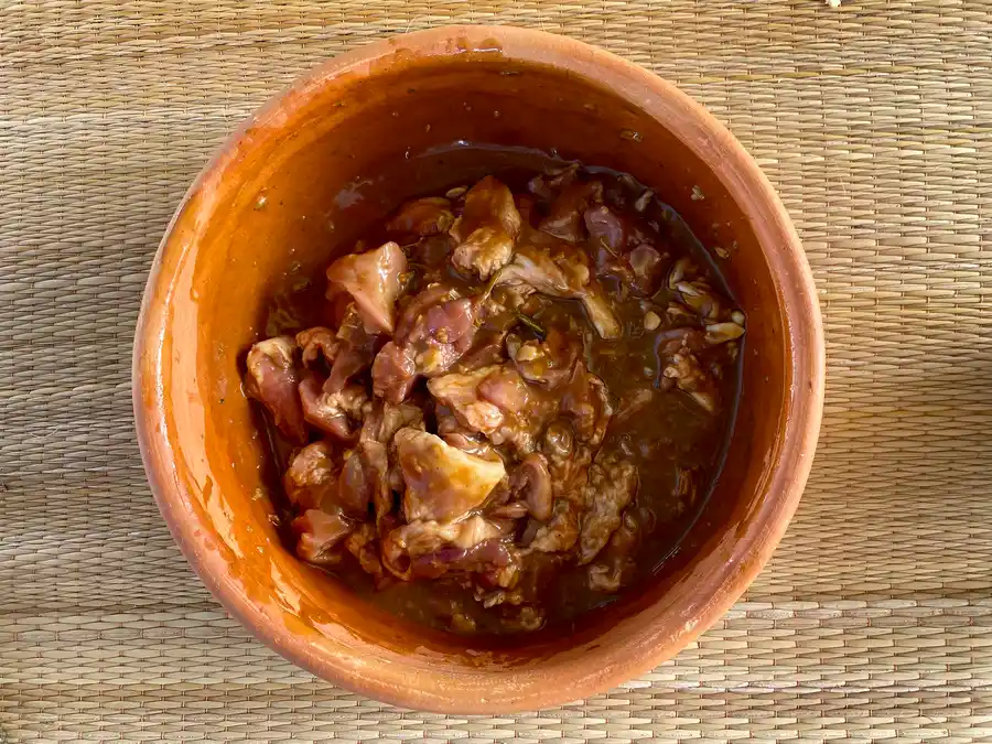 Thin slices of marinated pork in a large clay bowl.
