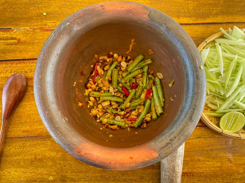 Som tam seasoning mixed with long beans and chilies in a mortar.