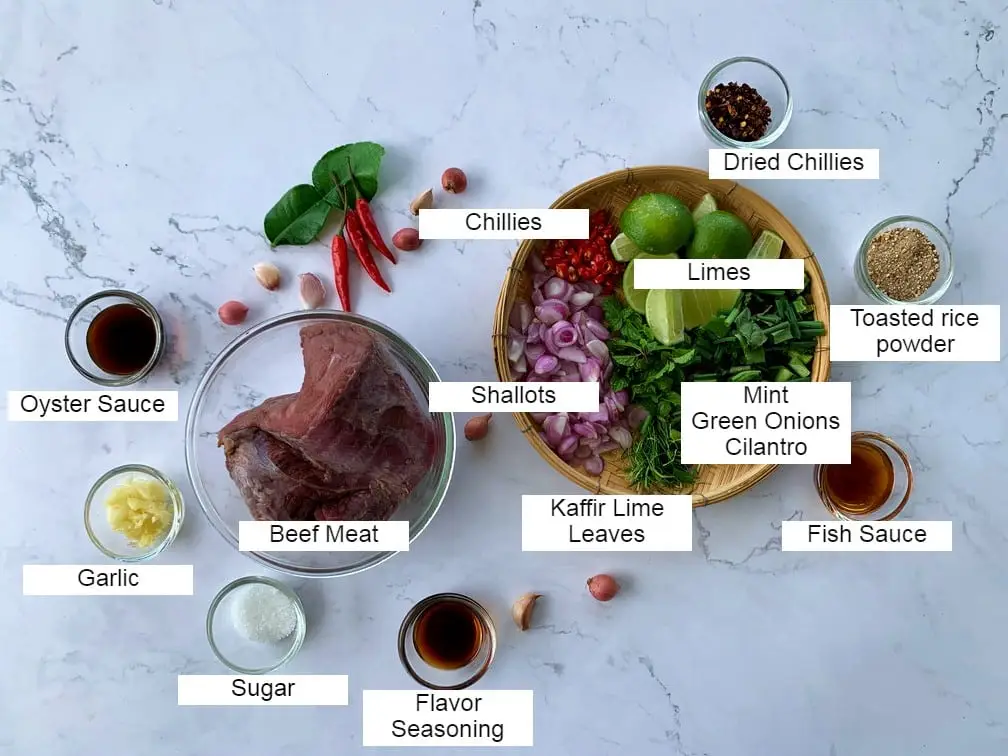 Top-view of nam tok beef ingredients with beef, lime, sauces and seasonings, and herbs.