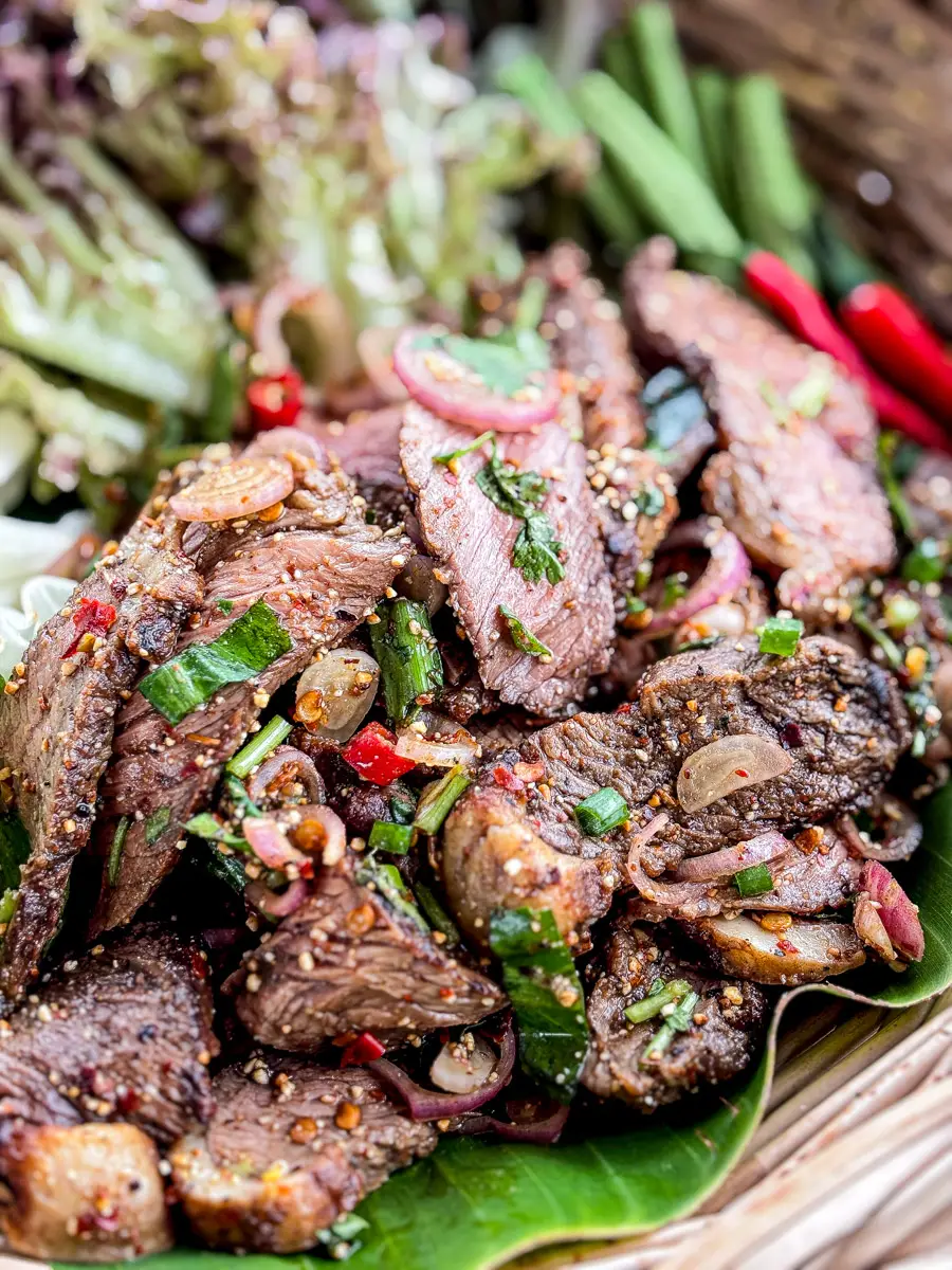 Close-up of Thai nam tok beef salad with grilled beef slices, red chilies, shallots, green onions, and herbs on a banana leaf.