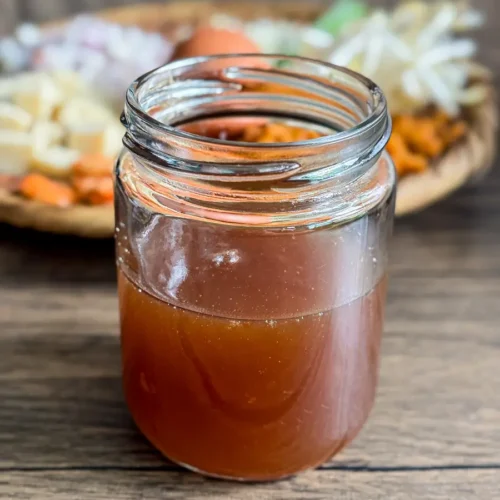 Homemade pad Thai sauce with a rich brown color, sitting on a wooden table, with fresh Thai ingredients blurred in the background.