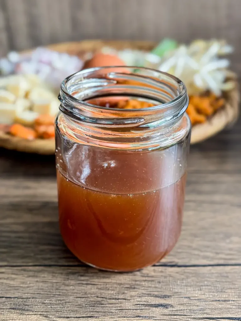 Homemade pad Thai sauce with a rich brown color, sitting on a wooden table, with fresh Thai ingredients blurred in the background.
