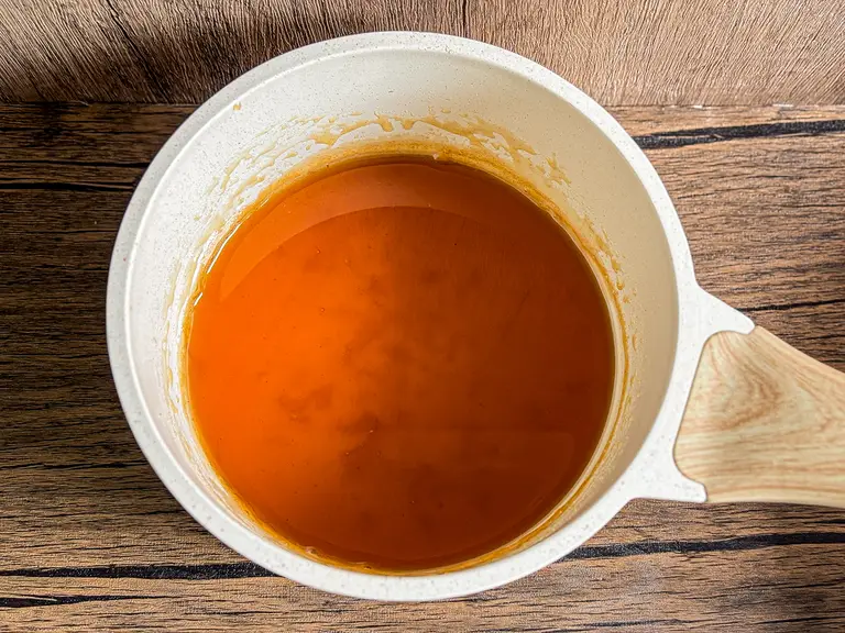 Freshly simmered pad Thai sauce in a white saucepan with a wooden handle, showing its glossy, rich orange-brown color.