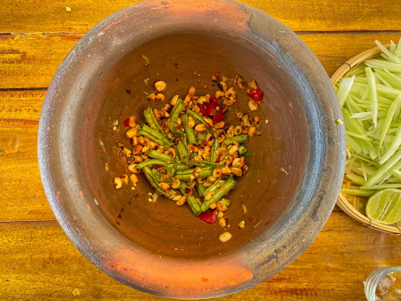 Long beans and roasted peanuts being pounded in a clay mortar.