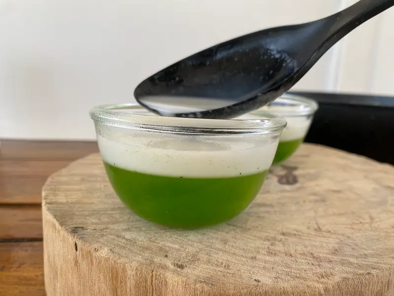 Gently spooning coconut jelly layer over the set pandan layer.
