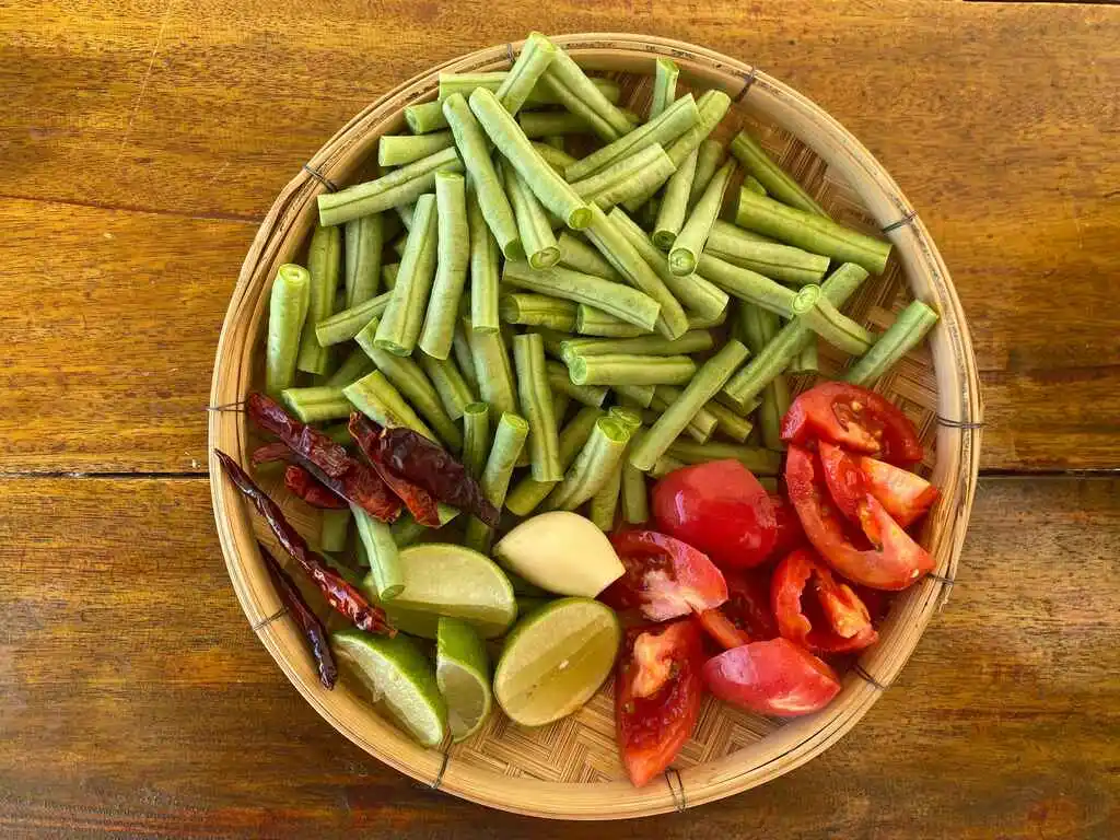 Fresh yardlong beans, tomatoes, lime, and chilies prepared for Thai long bean salad.
