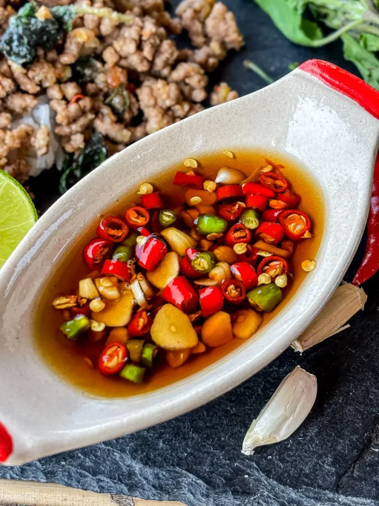 Overhead shot of prik nam pla in a white spoon dish, surrounded by fresh lime and garlic.