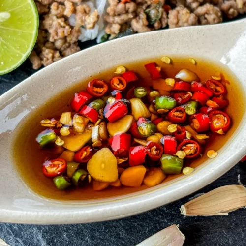Prik nam pla served in a ceramic dish with lime in the background.