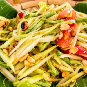 Close-up of som tam papaya salad with shredded green papaya, tomatoes, peanuts, and long beans in a sweet, sour, and spicy dressing.