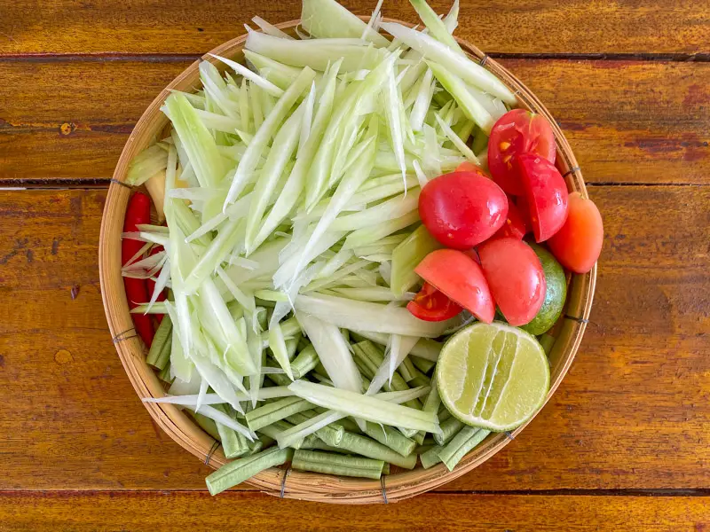 Overview of prepped green papaya, long beans, tomatoes, and lime.