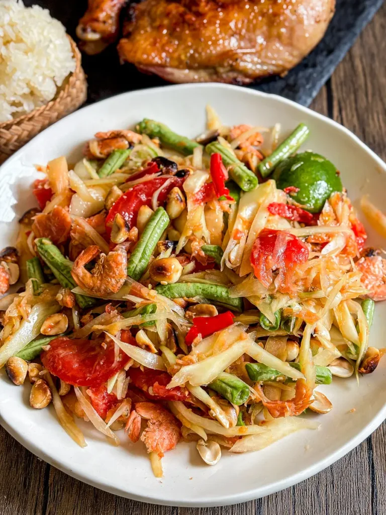 Som tam thai papaya salad with dried shrimp, peanuts, tomatoes, lime, sticky rice, and grilled chicken.
