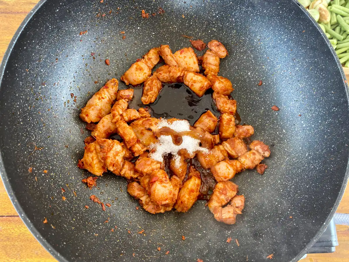 Top-down view of a wok with stir-fried bacon, red curry paste, and sauces and seasonings.