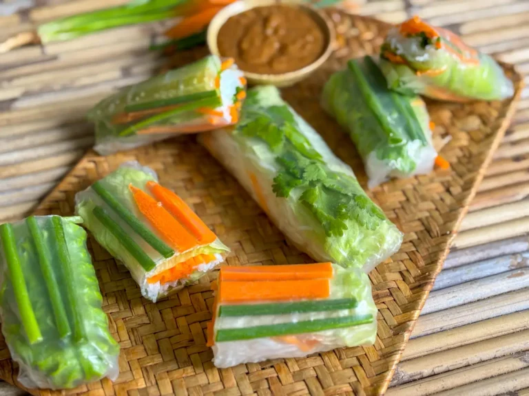 Thai fresh spring rolls with a colorful vegetable filling, arranged beside a bowl of peanut dipping sauce on a wooden platter.