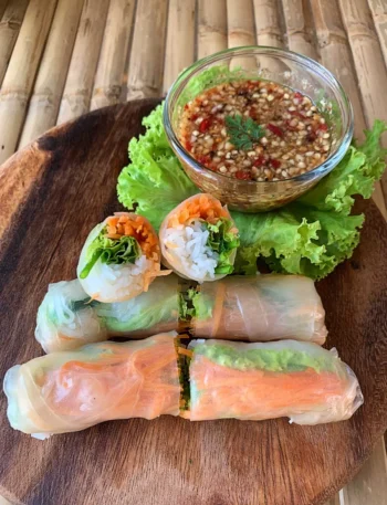 Thai fresh spring rolls with vibrant vegetables and rice noodles served with spicy dipping sauce on a wooden platter.