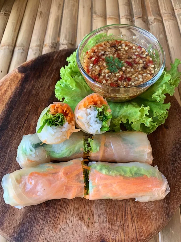 Thai fresh spring rolls with vegetables and rice noodles served with spicy dipping sauce on a wooden platter.