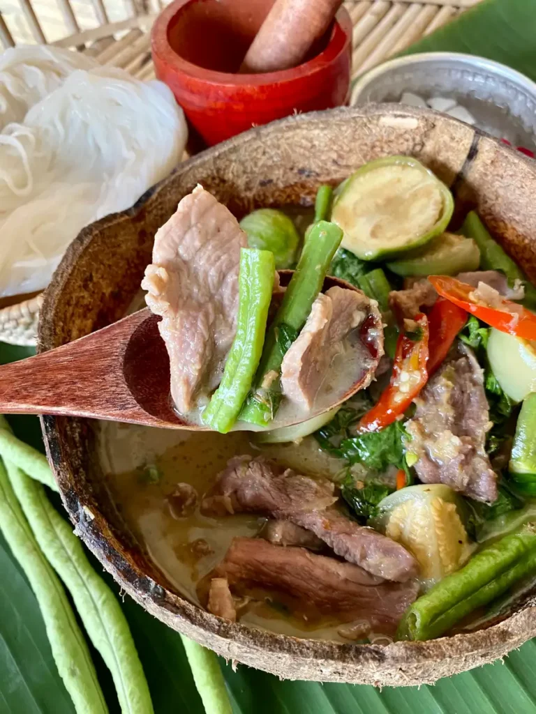 Close-up of Thai green curry pork, or gaeng keow wan, with slices of pork, yard-long beans, and Thai eggplants in a creamy curry served in a coconut bowl.
