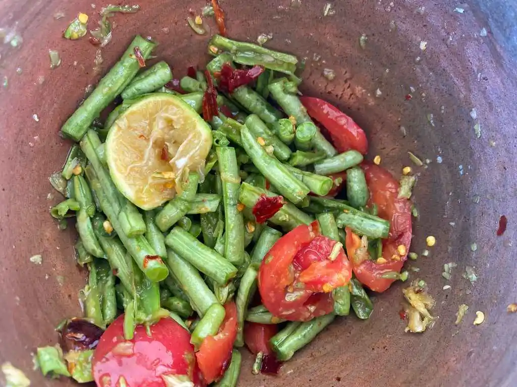 A mortar with Thai long bean salad with tomatoes and lime.
