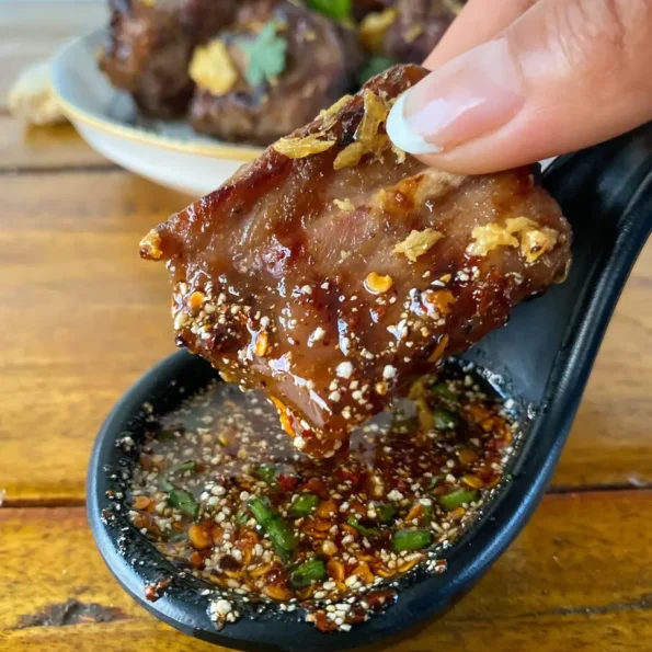 Hand dipping grilled Thai ribs in a spicy dipping sauce.