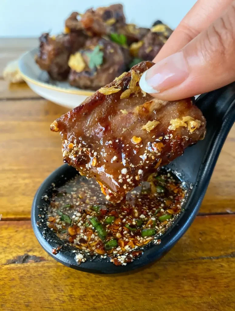 Hand dipping grilled Thai ribs in a spicy dipping sauce.