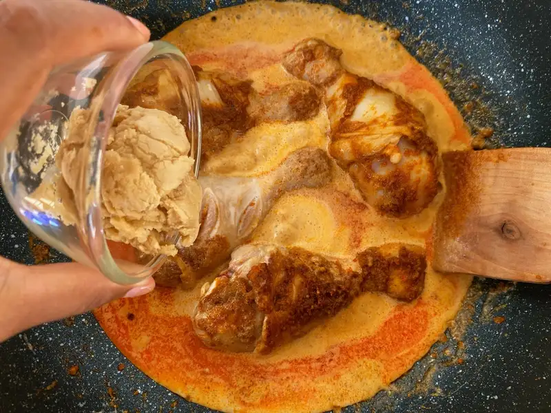 Adding palm sugar to massaman curry with chicken in a pan.
