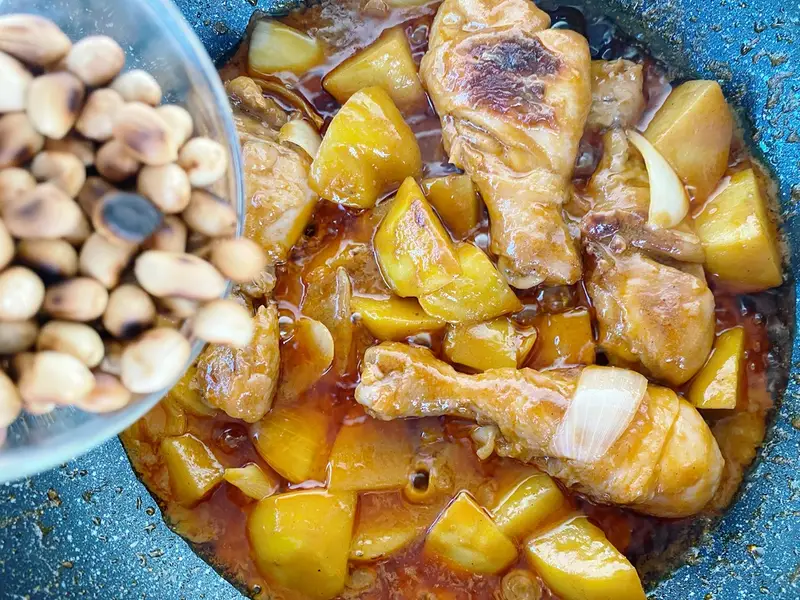 Adding roasted peanuts to massaman chicken curry with potatoes and chicken.