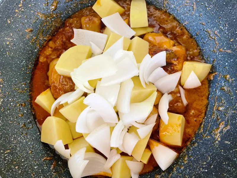 Adding potatoes and onions to massaman chicken curry in a pan.