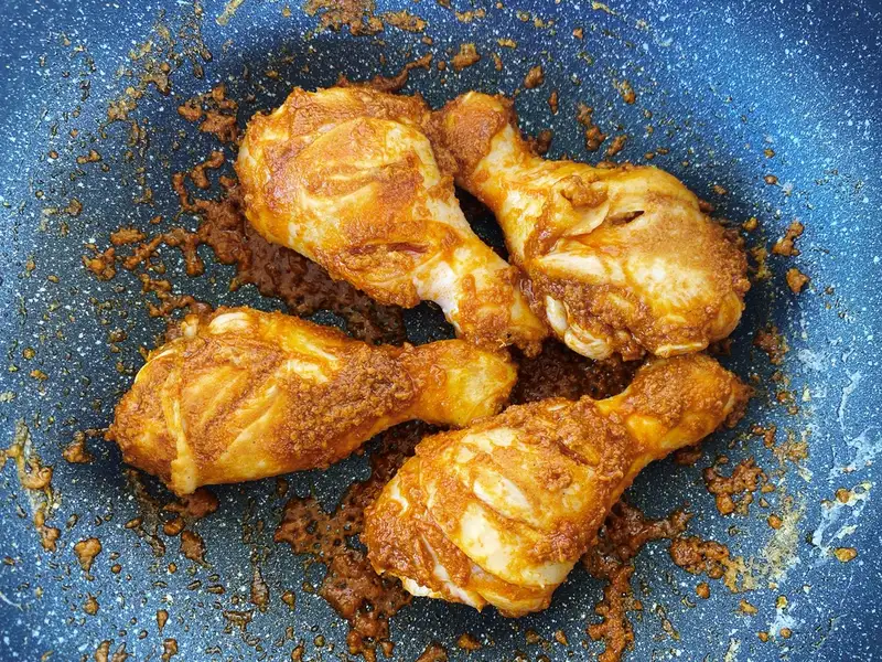 Chicken drumsticks coated in massaman curry paste in a pan.