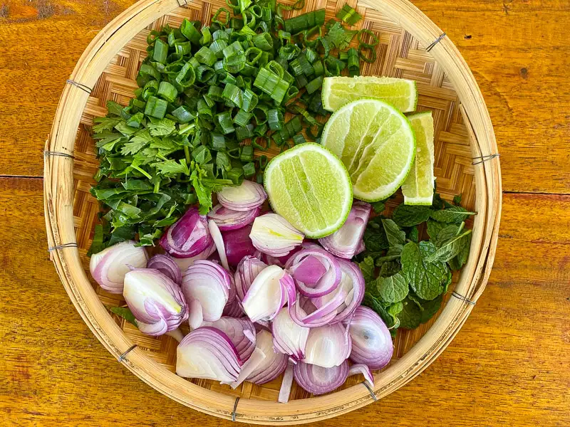 Chopped green onions, herbs, sliced shallots, and lime on a tray.