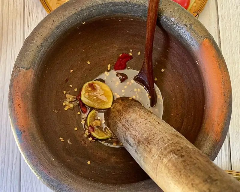 Making tam sua dressing in mortar with lime chilies and garlic.