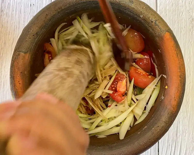 Mixing shredded green papaya with dressing in mortar.