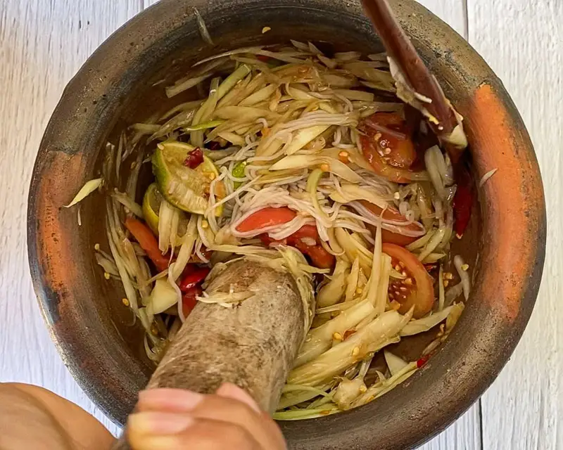 Adding rice vermicelli noodles to papaya salad in mortar.
