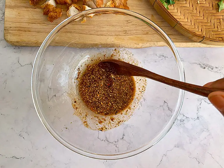 Larb dressing with chili flakes and toasted rice powder in a mixing bowl.