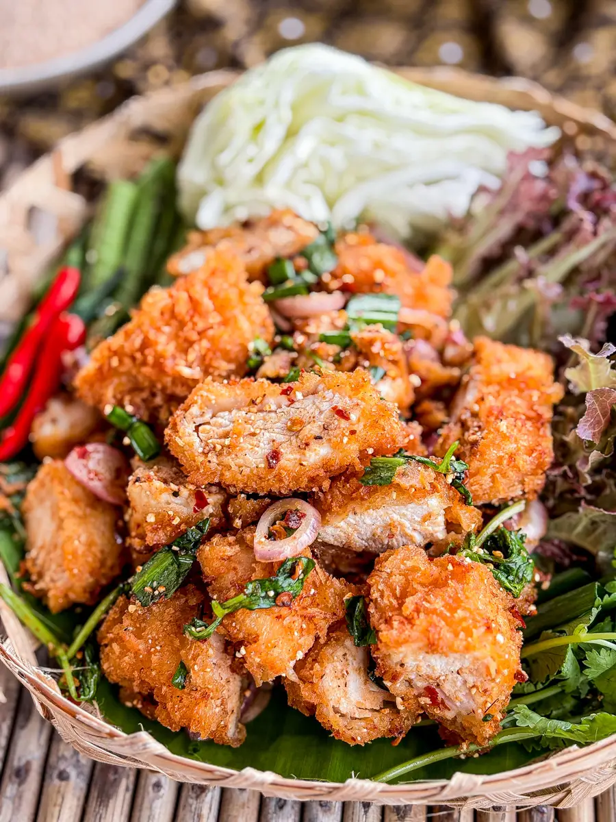 Crispy Thai fried chicken larb (larb gai tod) served on a woven tray with fresh herbs, cabbage, long beans, and red chili.