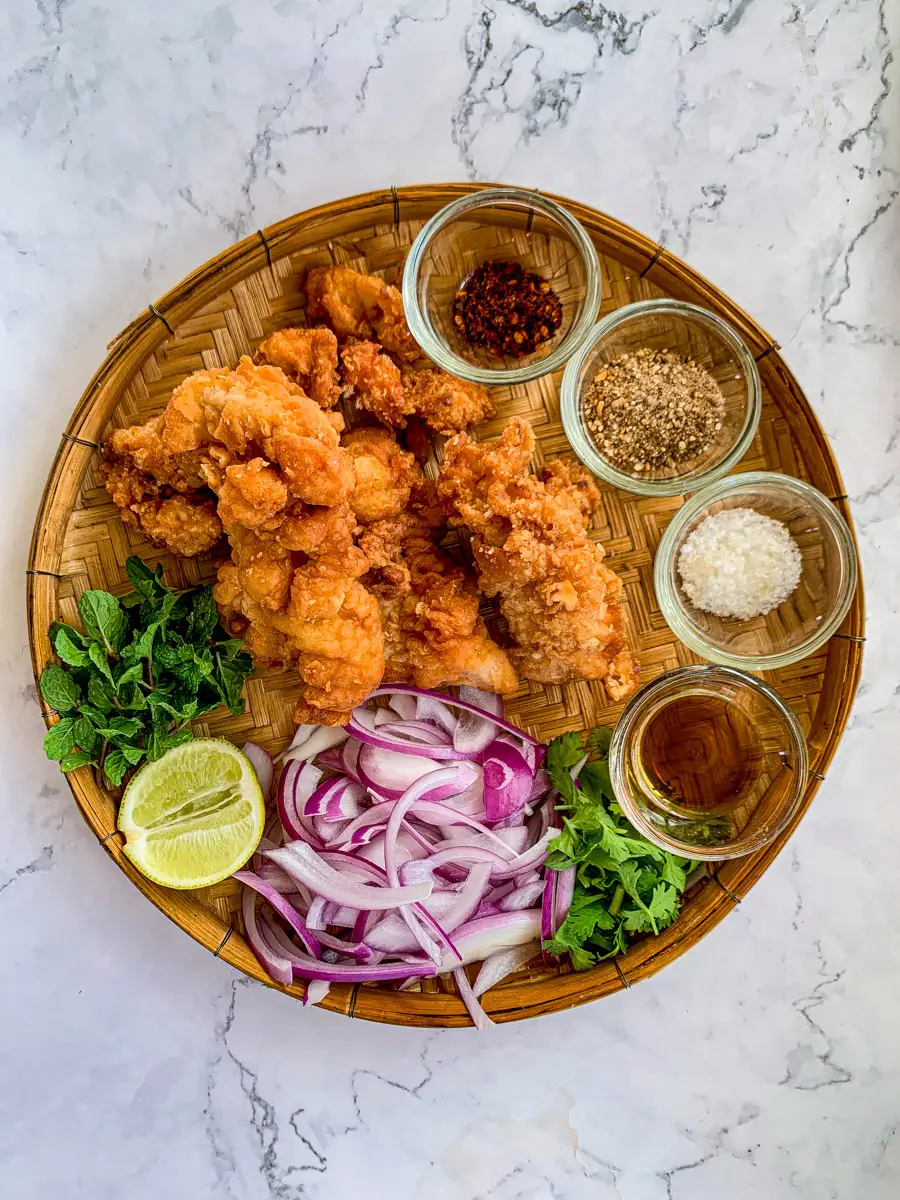 Ingredients for larb gai tod including fried chicken, sliced shallots, mint, lime, and small bowls of seasoning.