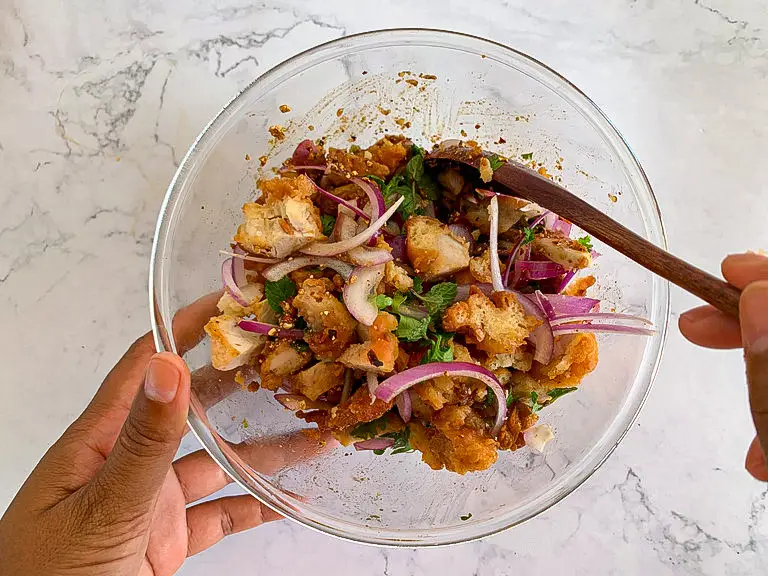 Mixing fried chicken with shallots and herbs in a glass bowl.