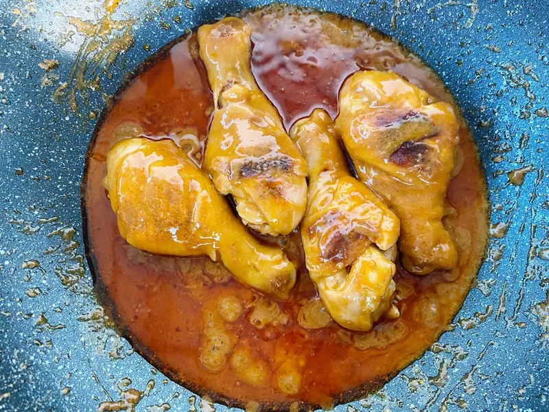 Chicken drumsticks simmering in massaman curry sauce in a pan.