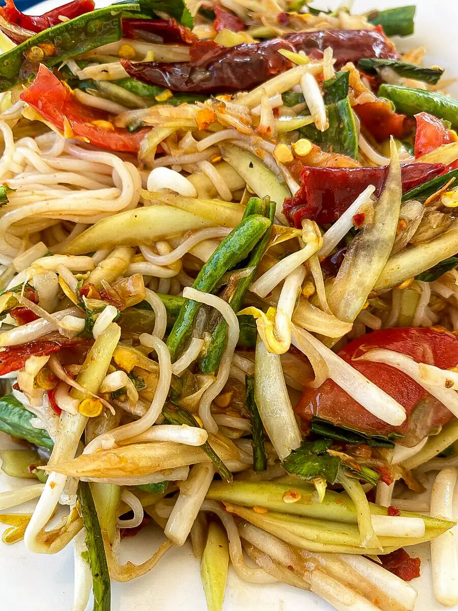Spicy Thai rice vermicelli papaya salad with long beans, chilies, tomatoes, and dried shrimp mixed with green papaya and lime dressing.