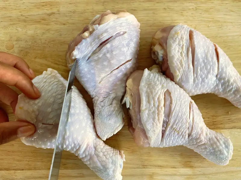 Cutting slits into chicken drumsticks to help them cook evenly.
